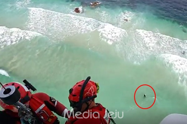 지난 25일 오후 애월 한담해변에서 제주해경 헬기 구조대가 바다에 빠진 관광객 A씨(붉은 색 원 안)를 구조하기 위해 호이스트를 이용해 내려가고 있다. [제주지방해양경찰청]